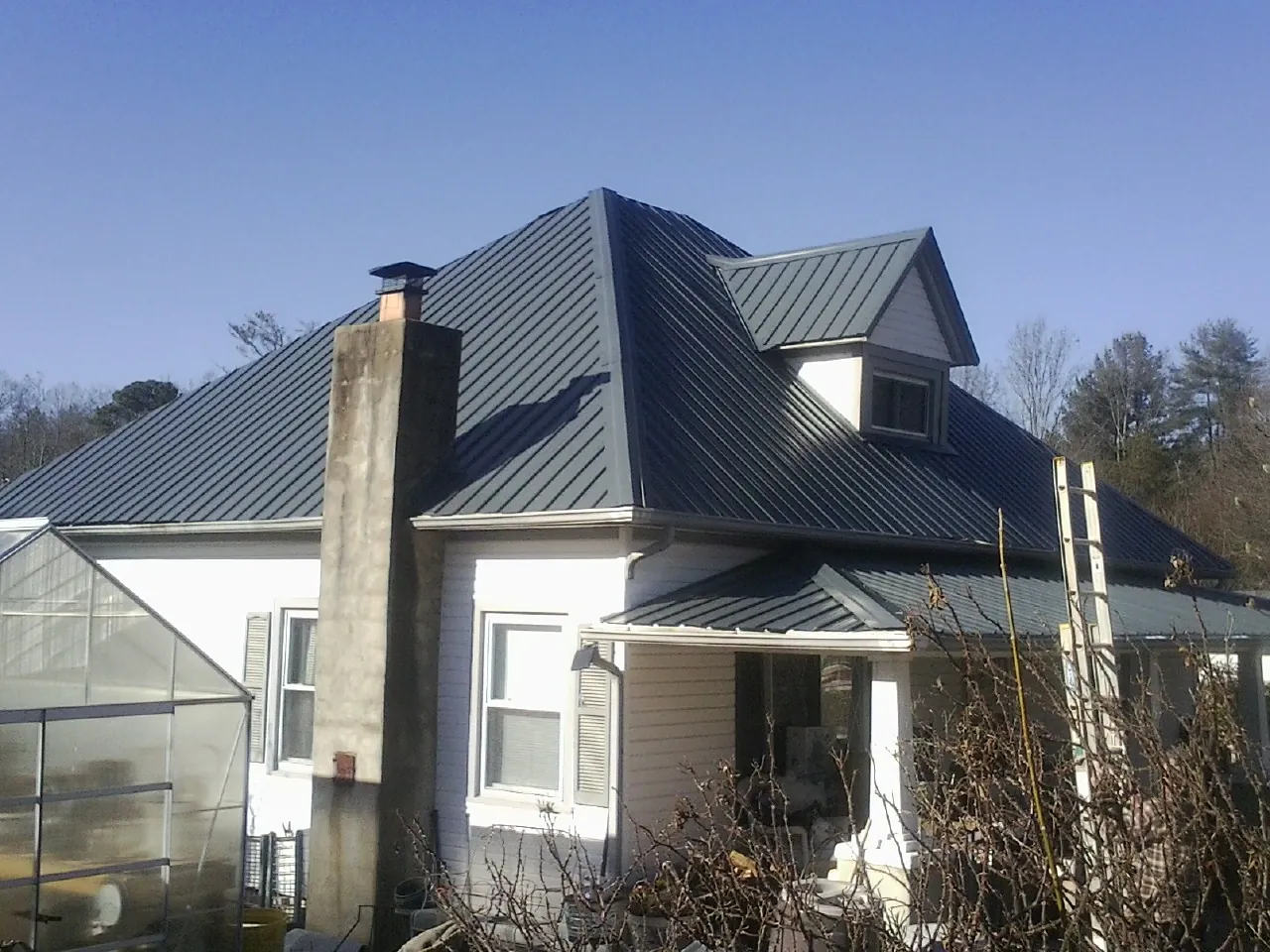 Dark blue standing seam metal roof on a white farmhouse with dormer — Slate & Tile Roof Repair by Roofing Brothers in Deer Trail