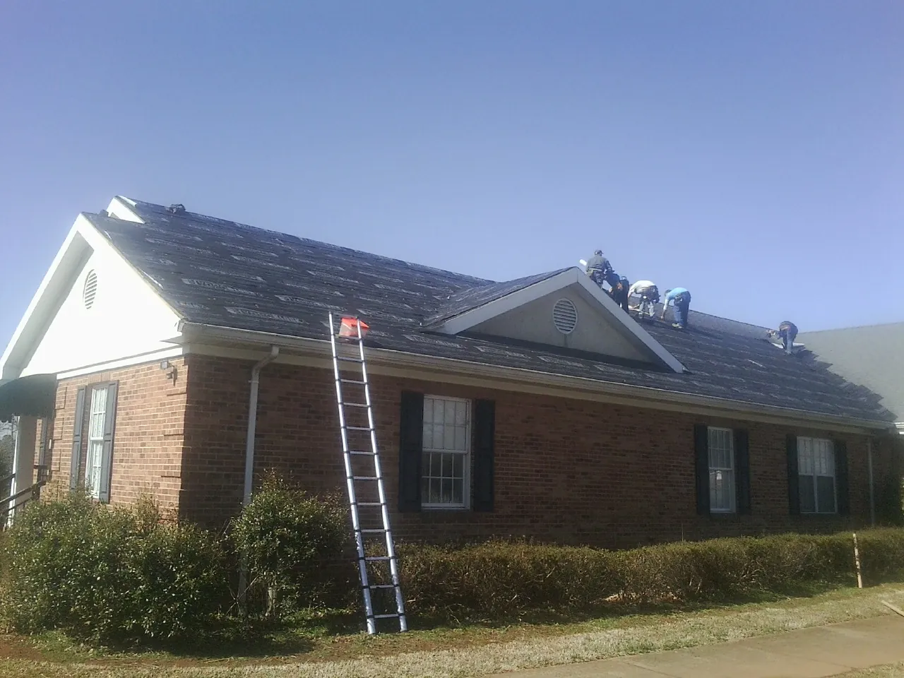 Crew tearing shingles off a brick ranch roof with a ladder set — Emergency Roof Repair work by our crew in Deer Trail