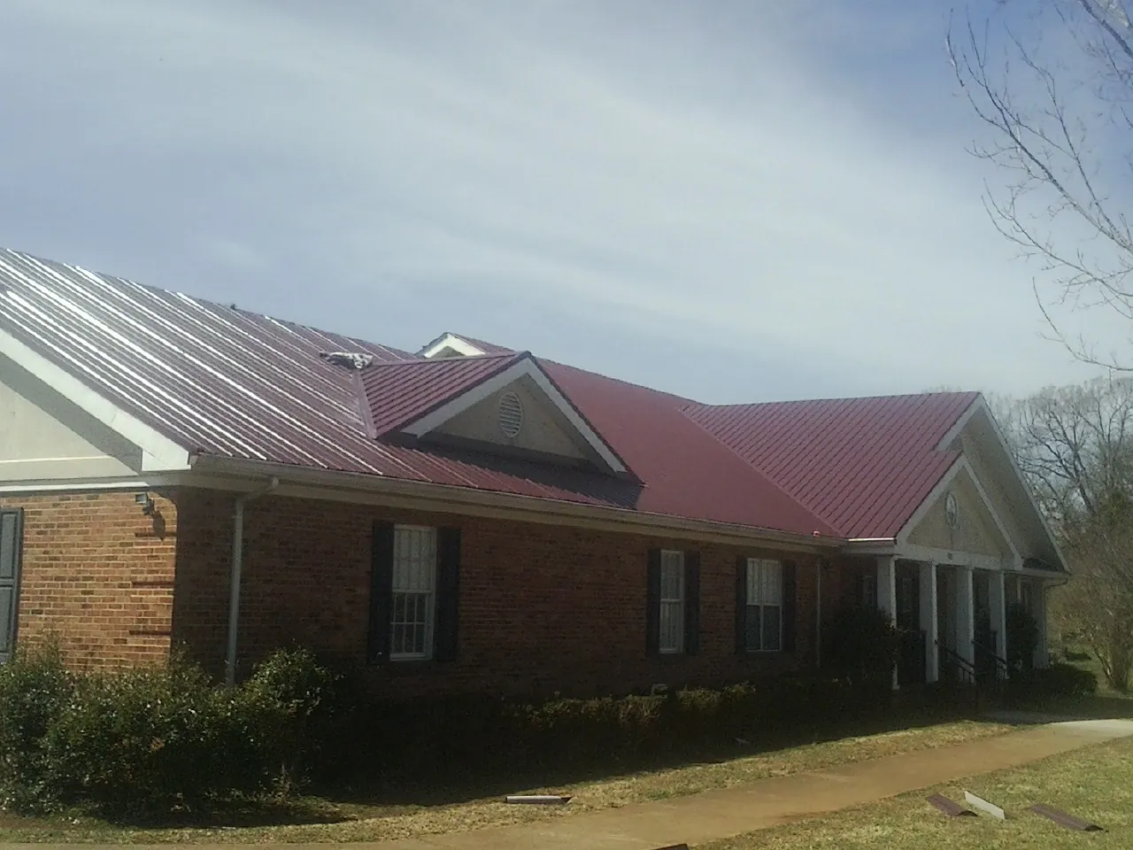 Red metal roof with gabled entries on a long brick building, from a Hail Damage Roof Repair job in Deer Trail