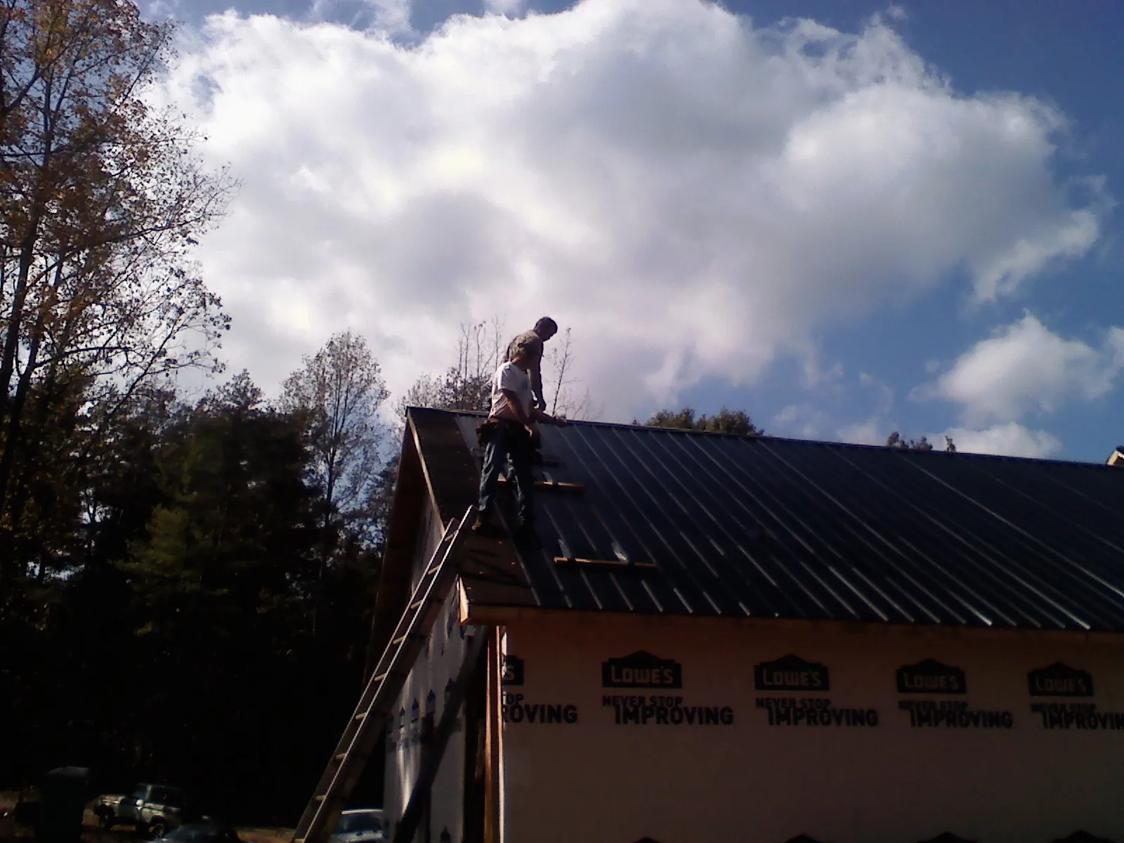 Roofer fastening dark metal panels high against a cloudy sky, from a Roof Inspection job in Deer Trail
