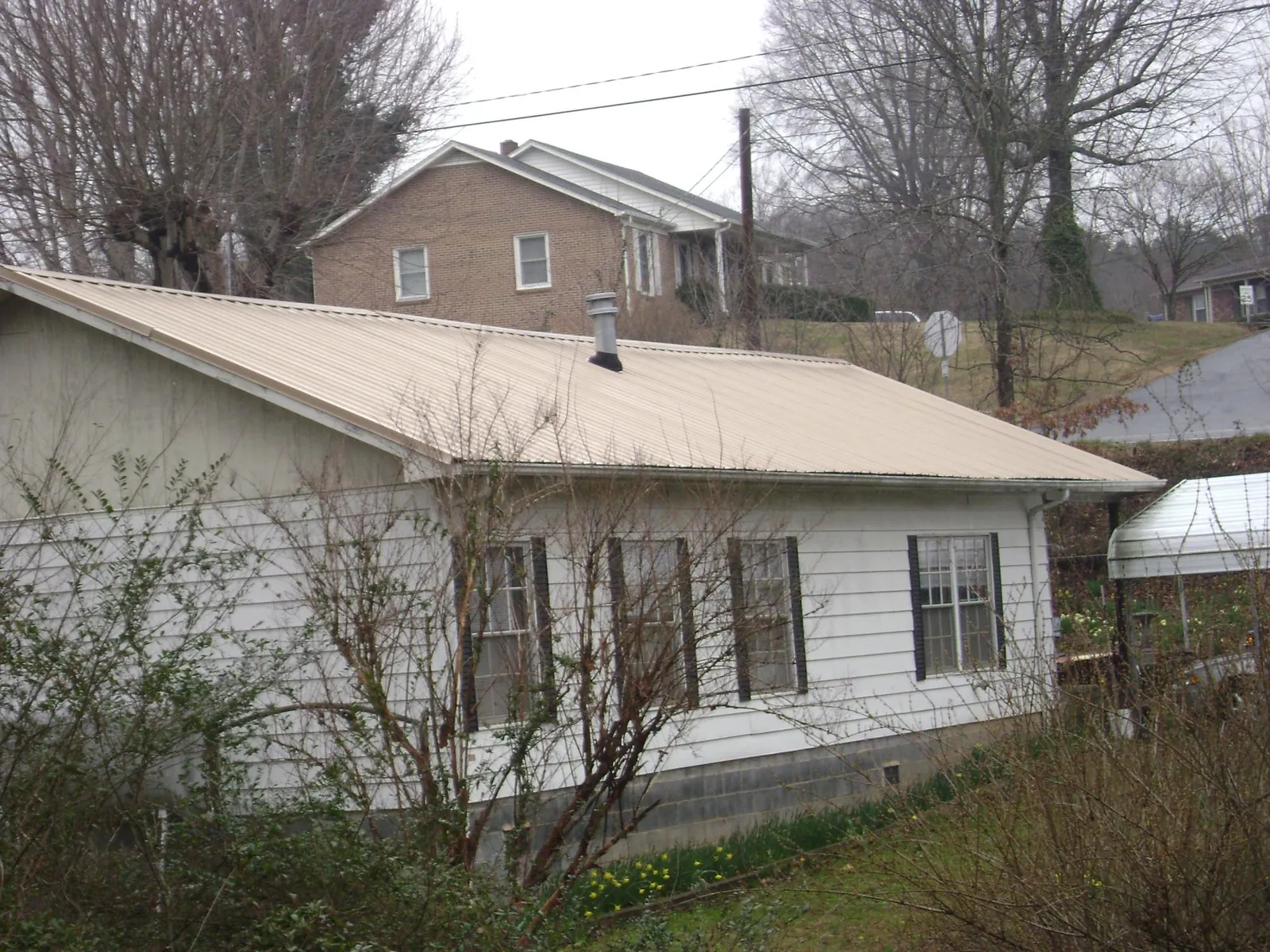 Tan metal roof on a white sided house set into a hillside — Commercial Roofing by Roofing Brothers in Deer Trail