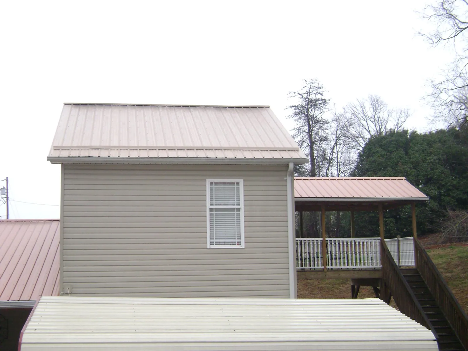 Tan metal roofs on a two story addition and attached porch, from a Roof Replacement job in Deer Trail